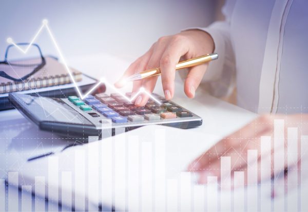 Accountant calculating profit with financial analysis graphs. Notebook, glasses and calculator lying on desk. Accountancy concept. Cropped view.